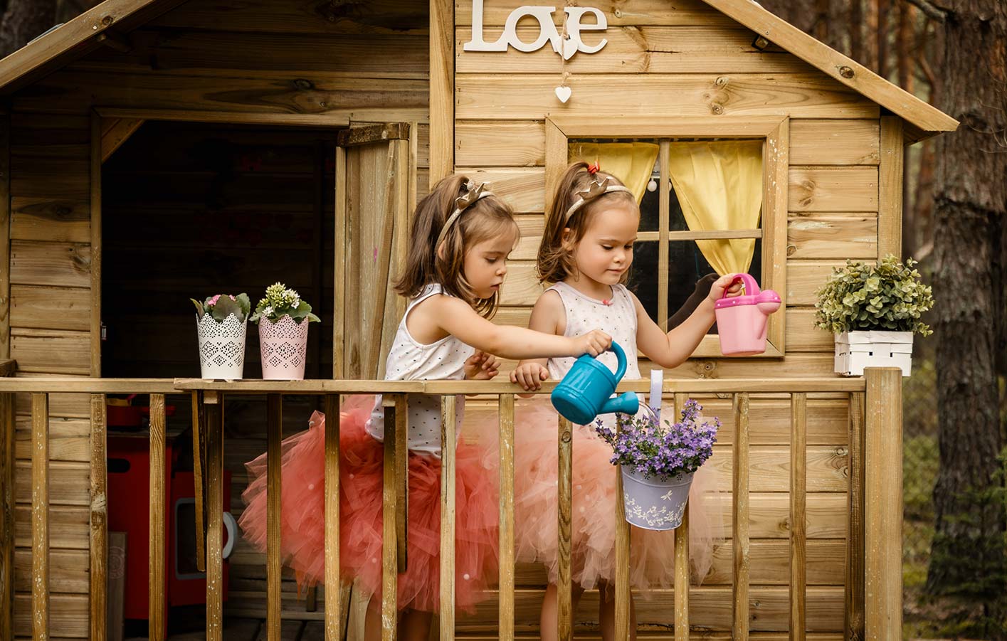 Zwei Mädchen gießen die Blumen vor ihrem Spielhaus
